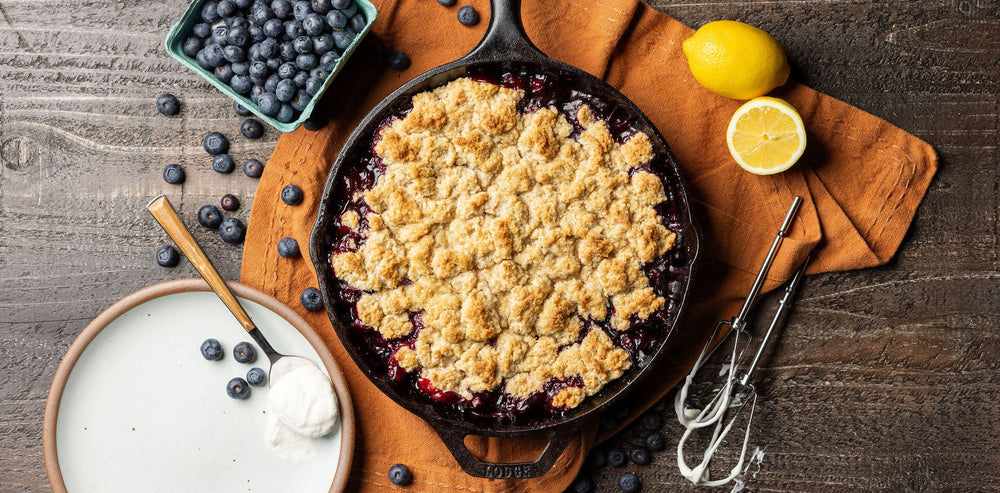 Cobbler served in skillet alongside extra blueberries and lemon wedges.