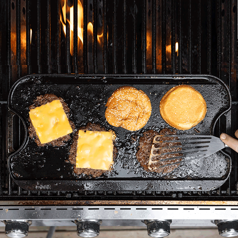 Grilling cheeseburgers and buns on a griddle over grill.