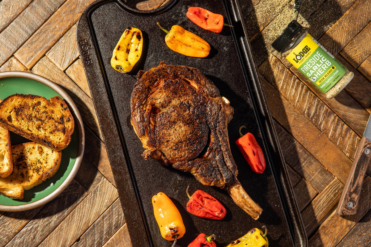 Grilled steak on a griddle with grilled bread and peppers on a wooden surface.