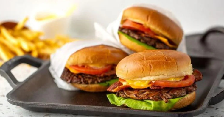 Three burgers on a griddle with fries in the background