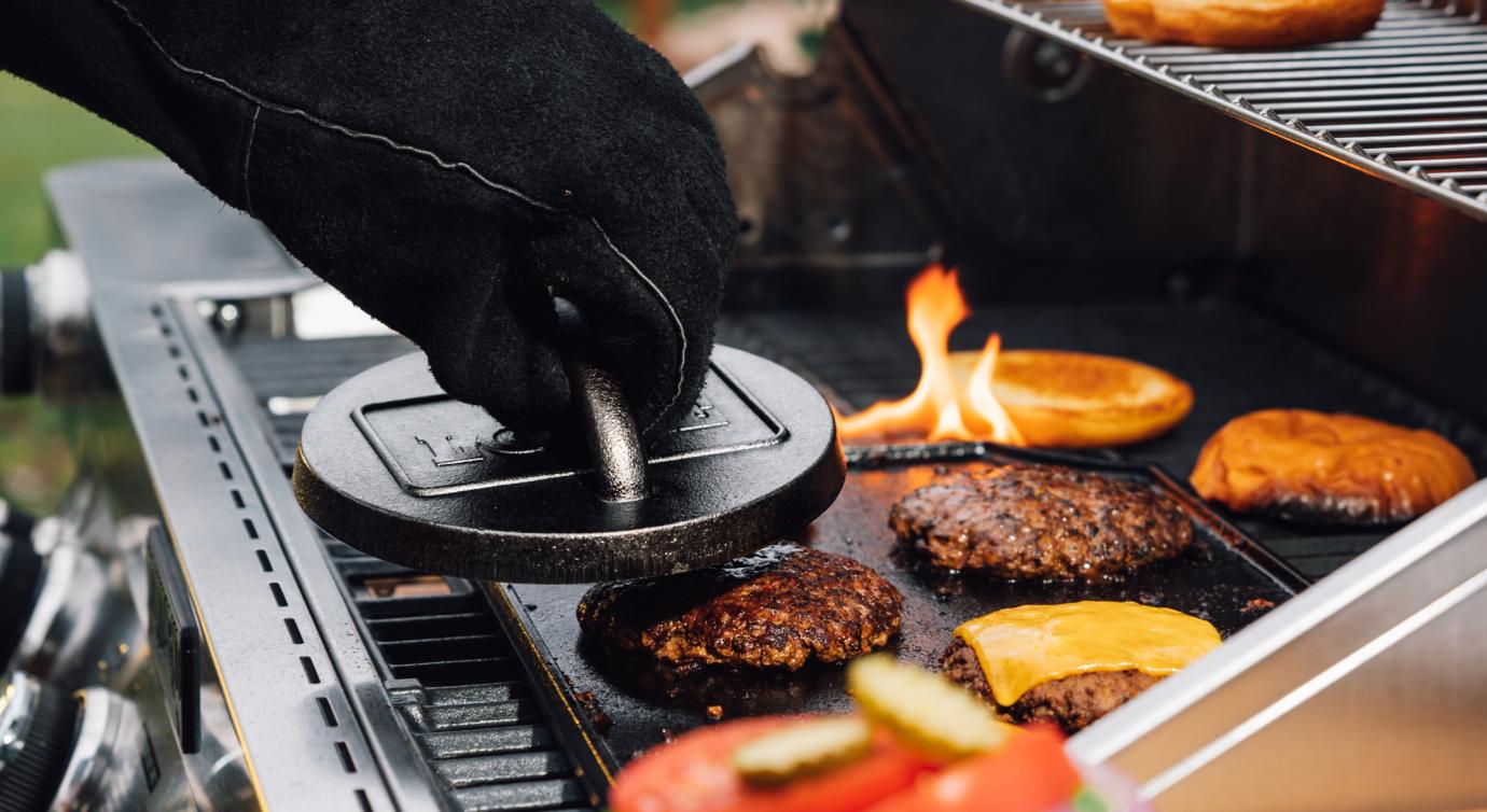 Someone using grill press to make smash burgers