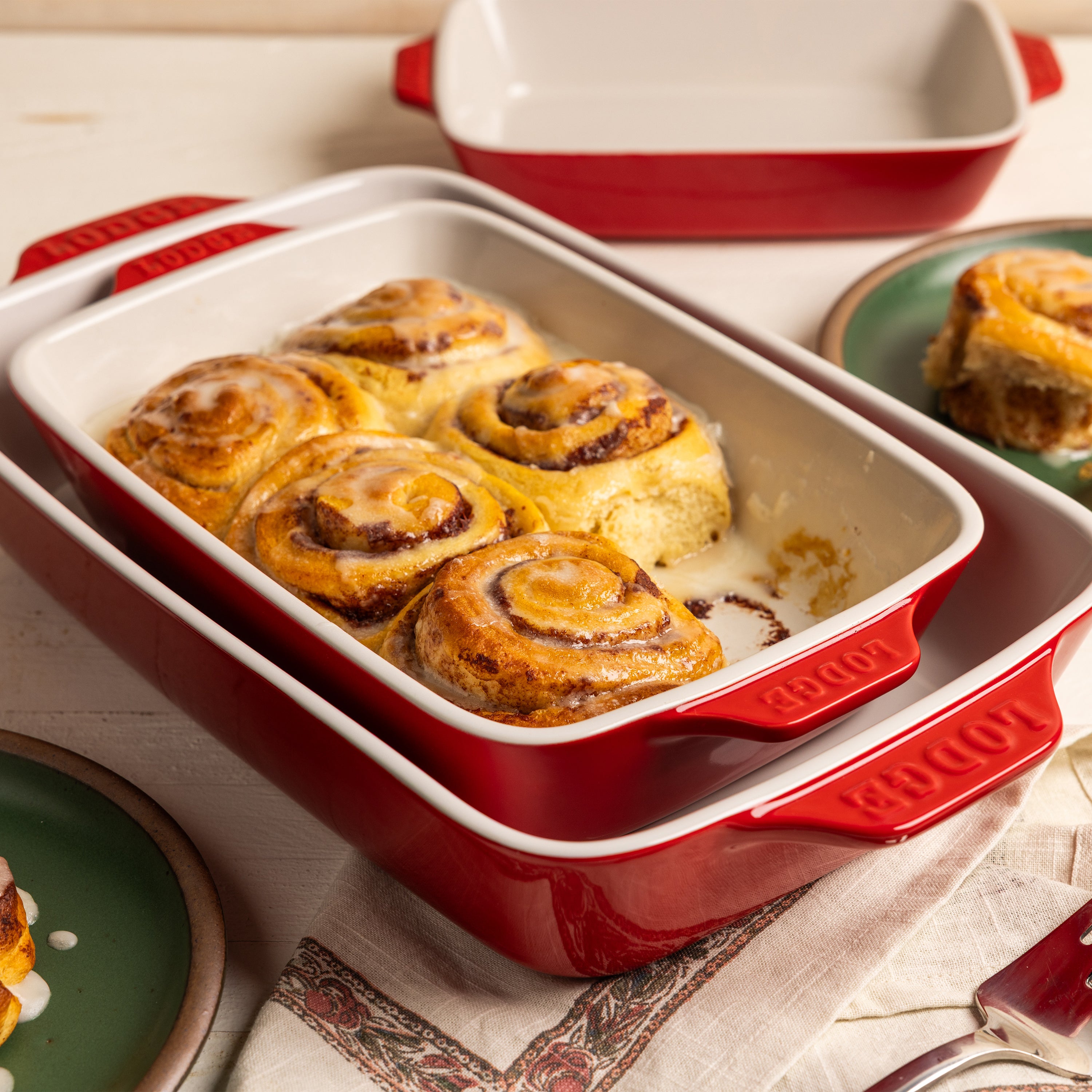 Partially served, baked cinnamon rolls in red ceramic baking dish.