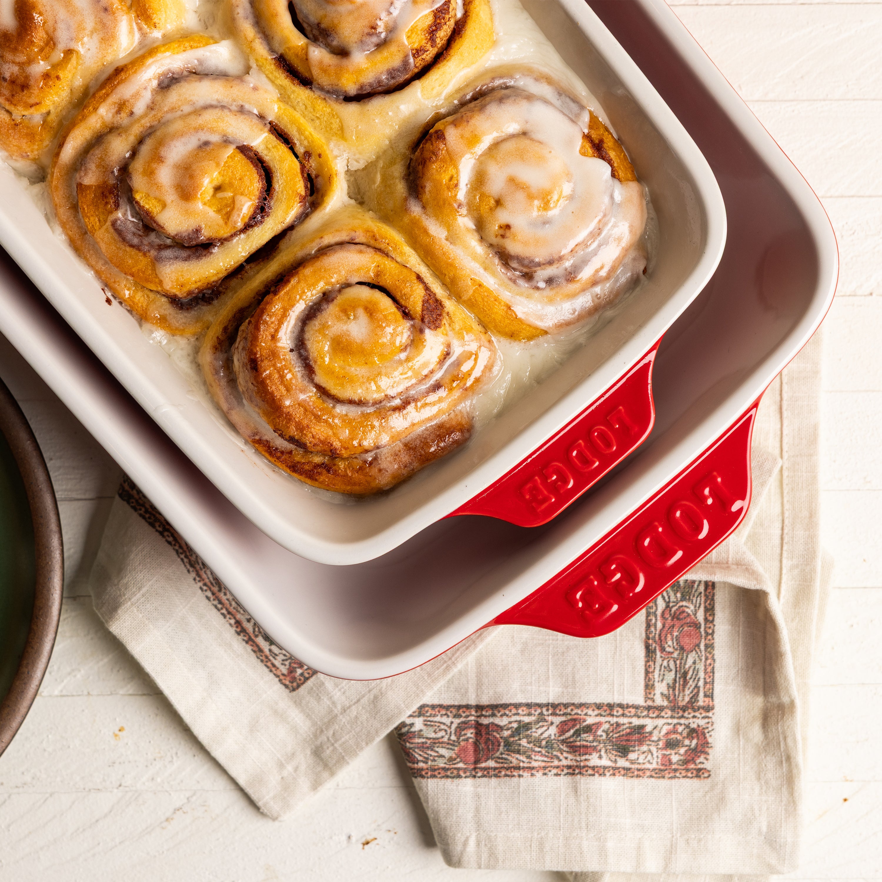Cinnamon rolls with icing in a cherry red baking dish.