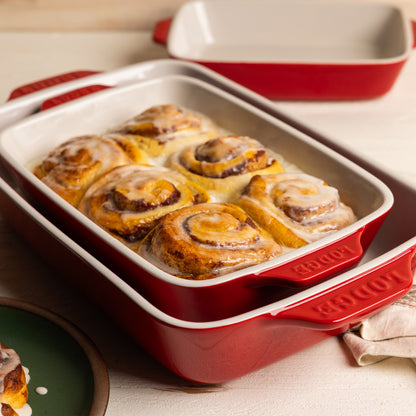 Nested, red ceramic baking dishes with cinnamon rolls.