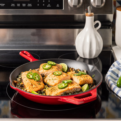 Red skillet with chicken and vegetables on a stovetop, with a white bottle in the background.