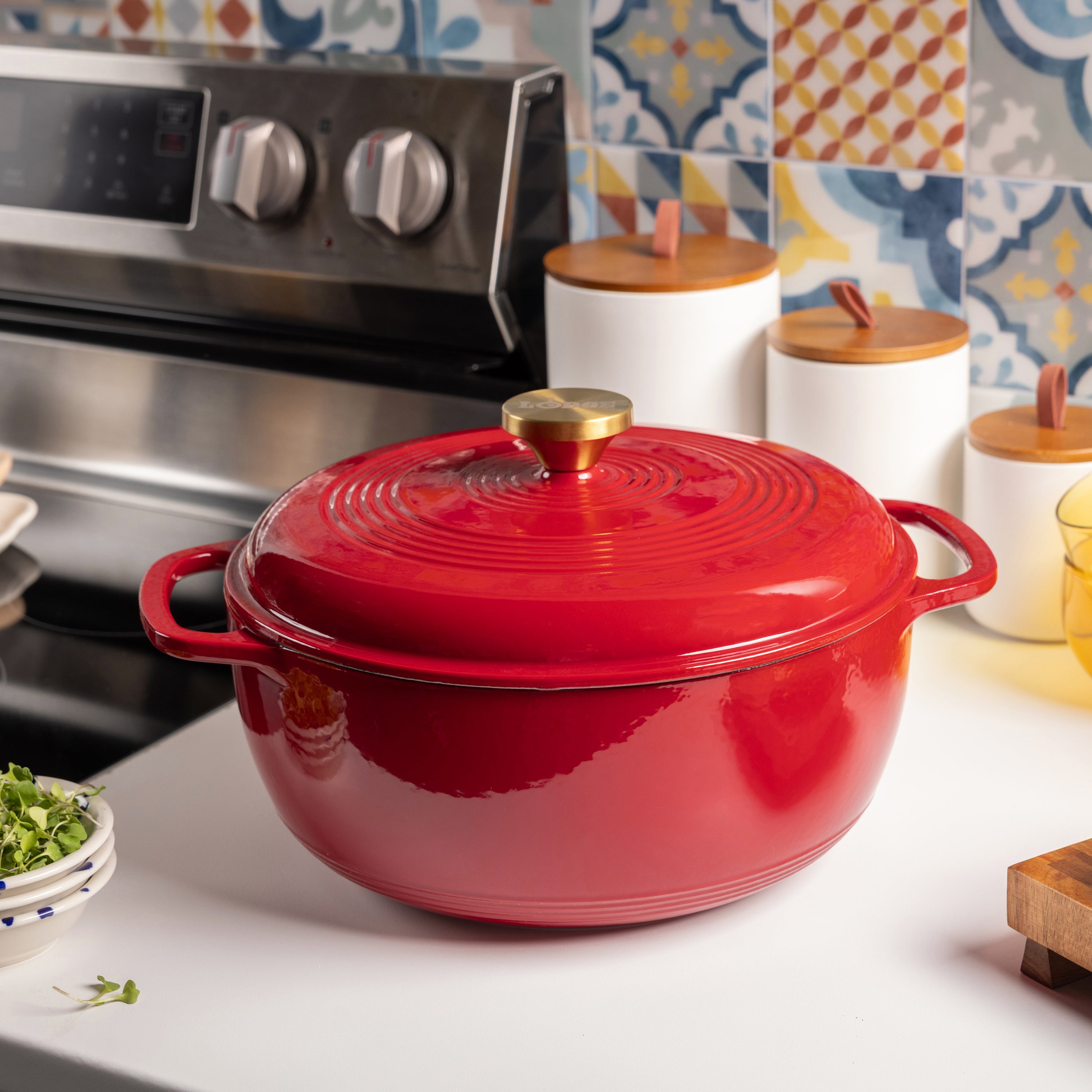 Red cast iron cookware on a kitchen counter with colorful tiles in the background