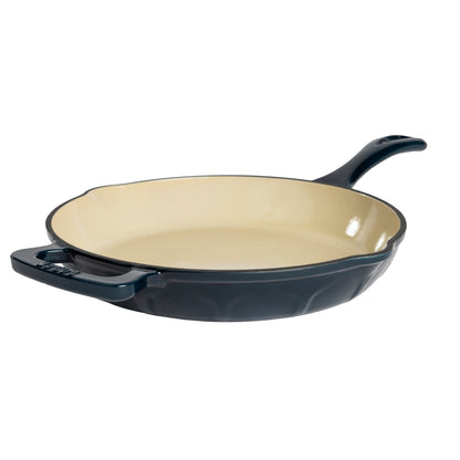 A blue enameled cast iron skillet with a cream-colored interior and a black rim, shown from a three-quarters angle on a white background.