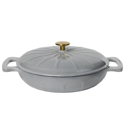 A light gray enameled cast iron lidded casserole dish with side handles, a gold-tone knob, and a sunburst pattern.