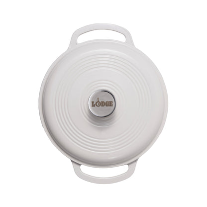 A white Lodge cast iron Dutch oven shown from a top-down view, featuring a circular lid with concentric ridges, two side handles, and a silver-colored center knob with the Lodge logo.