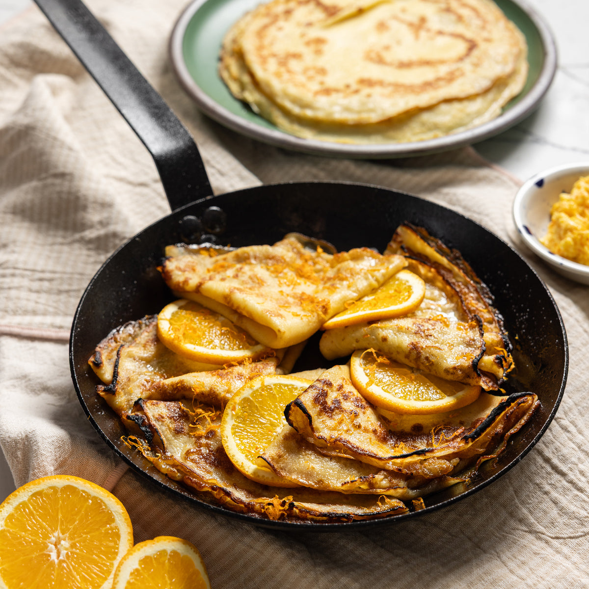 Freshly prepared crepes with orange butter and citrus sauce, made and served in skillet.