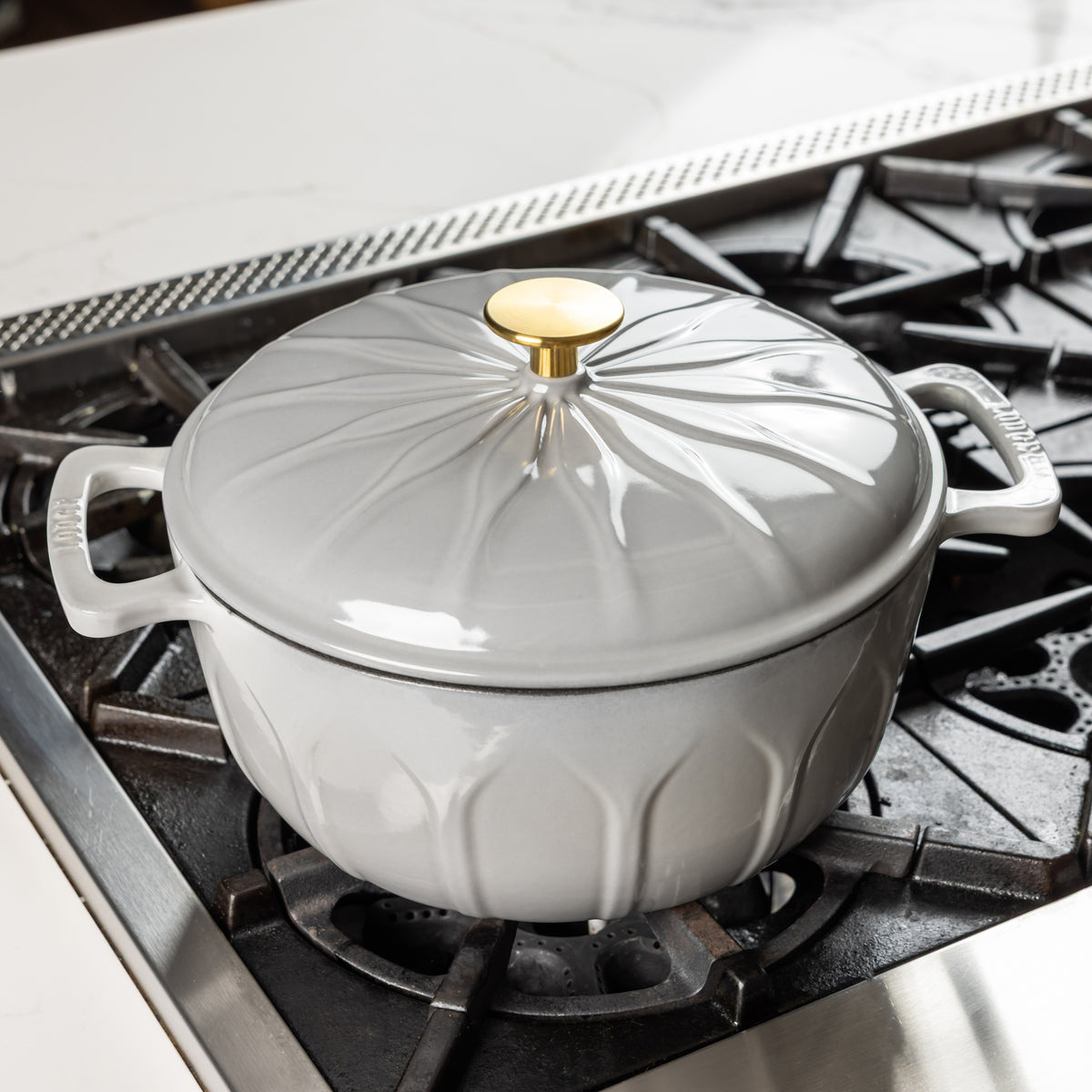 An enameled cast iron Dutch oven with a matching lid and gold-toned knob, shown sitting on a gas stovetop.