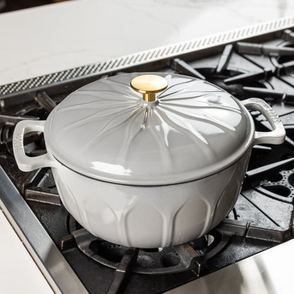 An enameled cast iron Dutch oven with a matching lid and gold-toned knob, shown sitting on a gas stovetop.