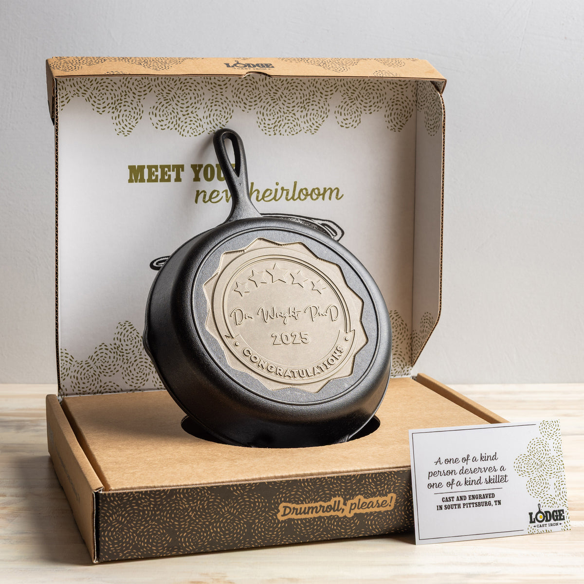 Cast iron skillet with engraved design in a decorative box on a wooden surface.