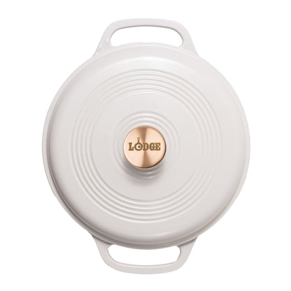 A top-down view of a white Lodge round cast iron Dutch oven lid with two handles and a copper center knob.