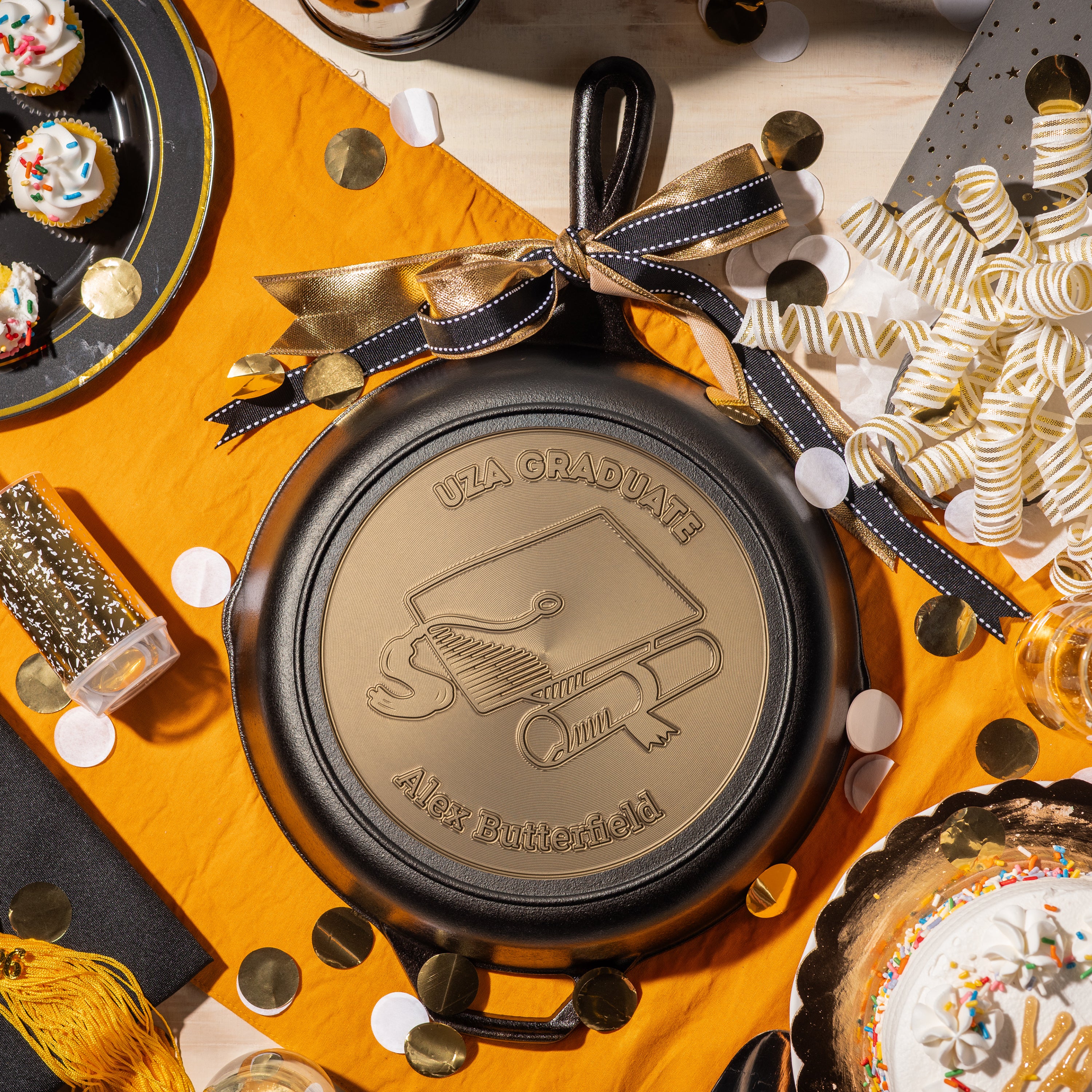 Graduation-themed personalized skillet on a festive background with confetti and small cakes.