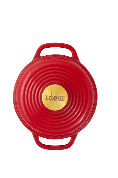 A red Lodge cast iron Dutch oven shown from a top-down view, featuring a circular lid with concentric ridges, two side handles, and a gold-colored center knob with the Lodge logo.