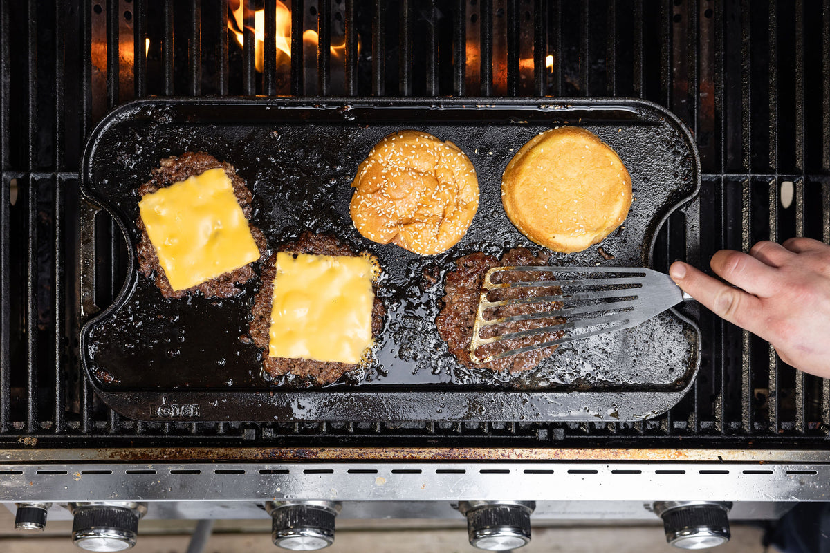 Grilling burgers with cheese and a spatula on a griddle over grill.
