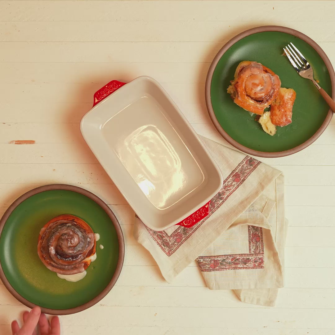 Fresh cinnamon rolls, served beside cherry red ceramic dish.