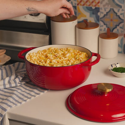 Someone sprinkling fresh herbs on mac and cheese, prepared and served in dutch oven.