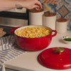 Someone sprinkling fresh herbs on mac and cheese, prepared and served in dutch oven.